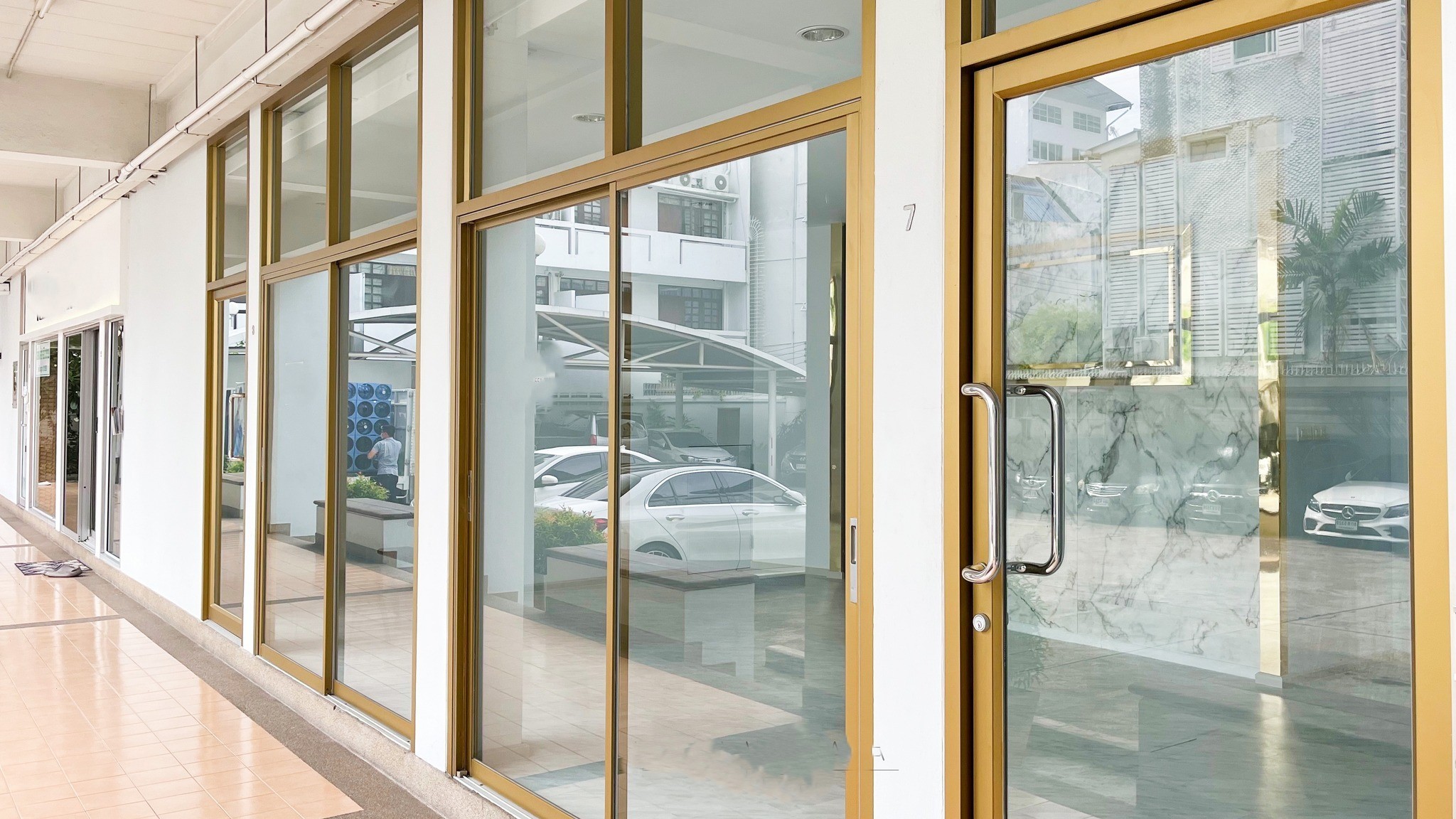 Retail Space for rent in Watthana, Bangkok - Street-facing glass storefront with gold-framed sliding doors under a covered arcade and onsite parking view.