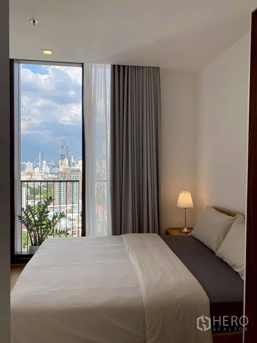 公寓 for rent in Watthana, Bangkok - 明亮卧室配双人床与台灯，落地窗外是城市景观。