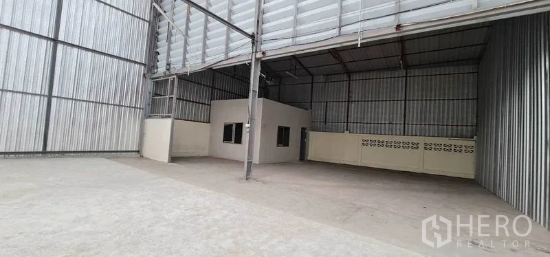 Warehouse for rent in Pak Kret, Nonthaburi - High‑ceiling warehouse interior with a small built‑in office and steel structure.