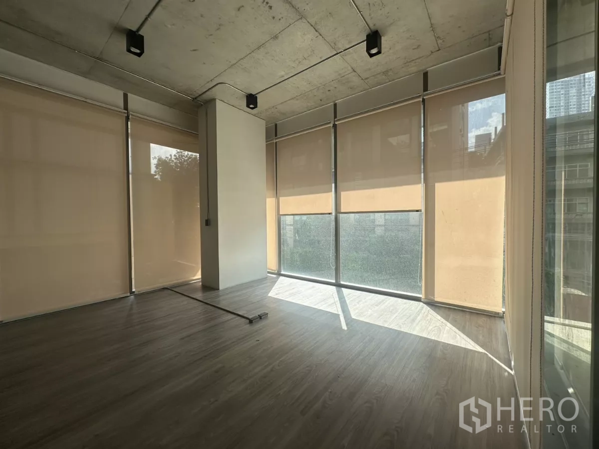 Retail Space for rent - Bright corner zone with beige roller blinds and wraparound floor-to-ceiling windows filtering natural light.