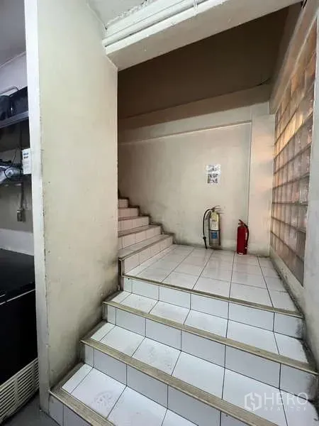 Shophouse for rent or sale in Khlong Toei, Bangkok - Interior tiled stairwell with fire extinguishers at the landing inside the shophouse.