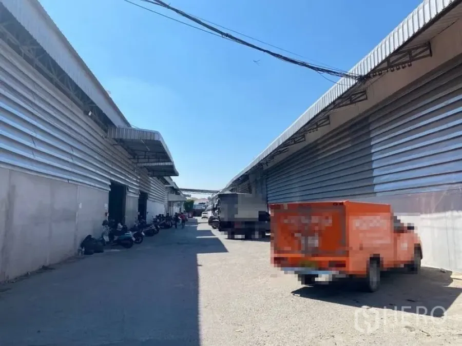 Warehouse for rent in Bueng Kum, Bangkok - Wide service lane between metal-clad warehouse blocks with loading bays and parking space for trucks and motorbikes.