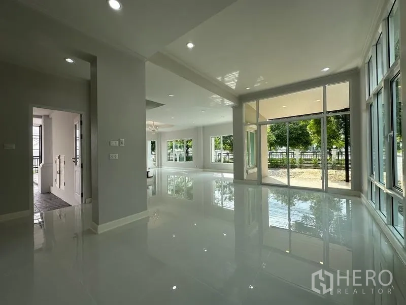 Detached House for sale in Lam Luk Ka, Pathum Thani - Bright open living area with glossy white tiles and floor-to-ceiling windows to the garden.