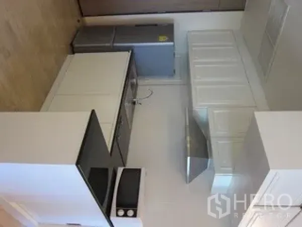 Condominium for rent in Khlong Toei, Bangkok - Compact kitchen with white cabinetry, cooktop, hood and stainless refrigerator.