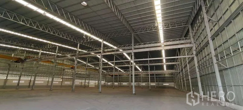 Warehouse for rent in Nikhom Phatthana, Rayong - Wide clear-span warehouse showing steel framing, overhead crane rails and bright roof lighting.
