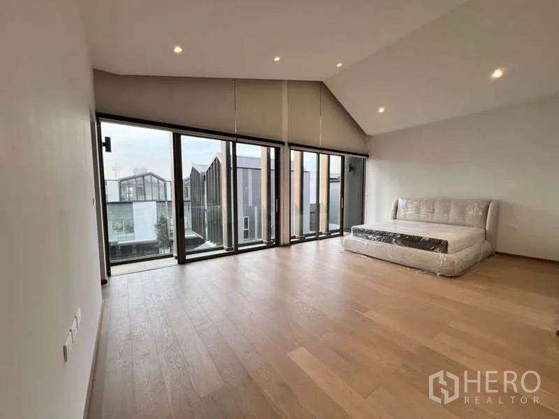 Townhouse for rent in Phra Khanong, Bangkok - Expansive bedroom with sloped ceiling and full-height glazing overlooking the neighborhood.