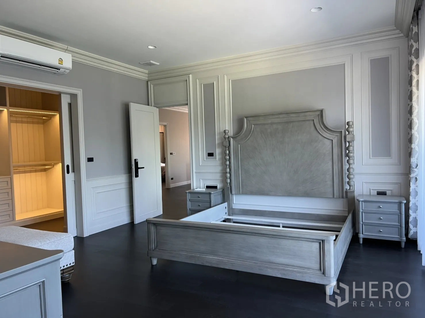 Detached House for rent or sale in Bang Kapi, Bangkok - Spacious master bedroom with paneled walls, classic bed frame and doorway to a walk-in closet, set on dark wood floors.