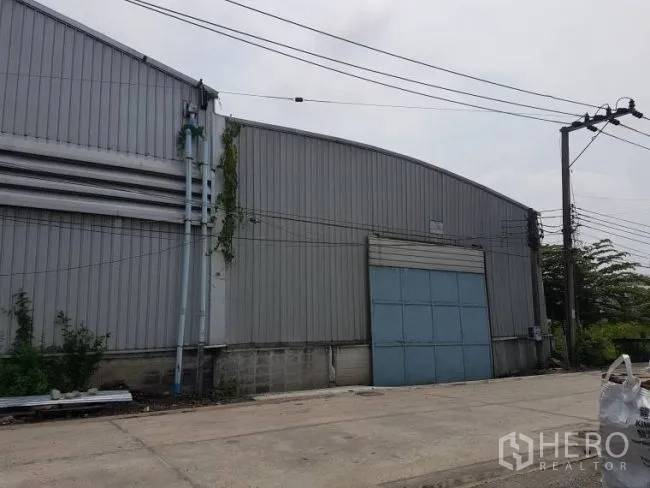 Factory for rent or sale in Bang Phli, Samut Prakan - Side elevation of the warehouse with arched roof and a large blue roller-shutter loading door.