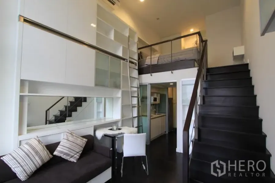 Condominium for rent in Khlong Toei, Bangkok - Double-height condo living space with tall storage, ladder and stairs to loft bedroom.