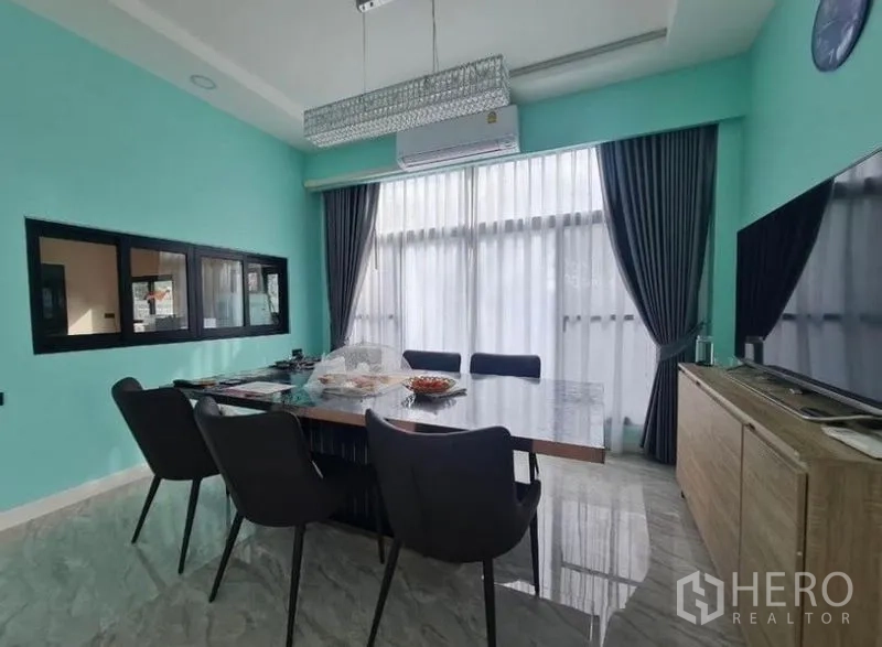 独立式住宅 出售在Sai Mai, Bangkok - 餐厅另一视角，长桌、薄荷绿色墙面与遮光窗帘。