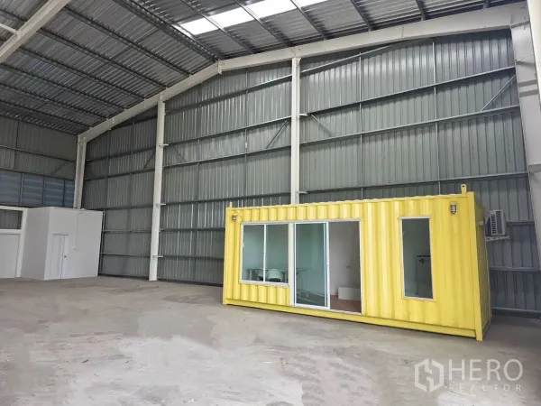Warehouse for rent in Khlong Luang, Pathum Thani - Spacious warehouse interior with high metal roof and a yellow container office with glass doors.
