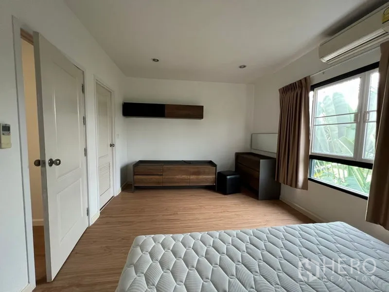 联排别墅 出租在Bang Kapi, Bangkok - 宽敞卧室，带低柜与窗外绿景。
