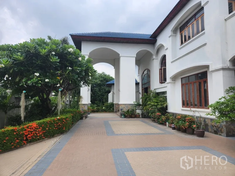 Detached House for rent in Prawet, Bangkok - Front approach with arched porch, landscaped hedges and a wide tiled driveway.