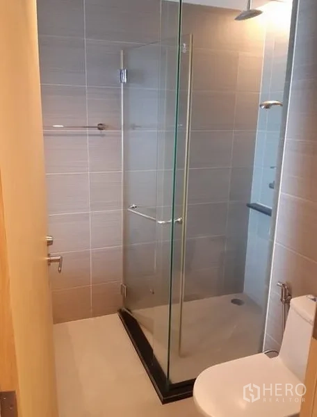 Condominium for rent in Khlong Toei, Bangkok - Second bathroom with walk-in glass shower and toilet in neutral tiles.