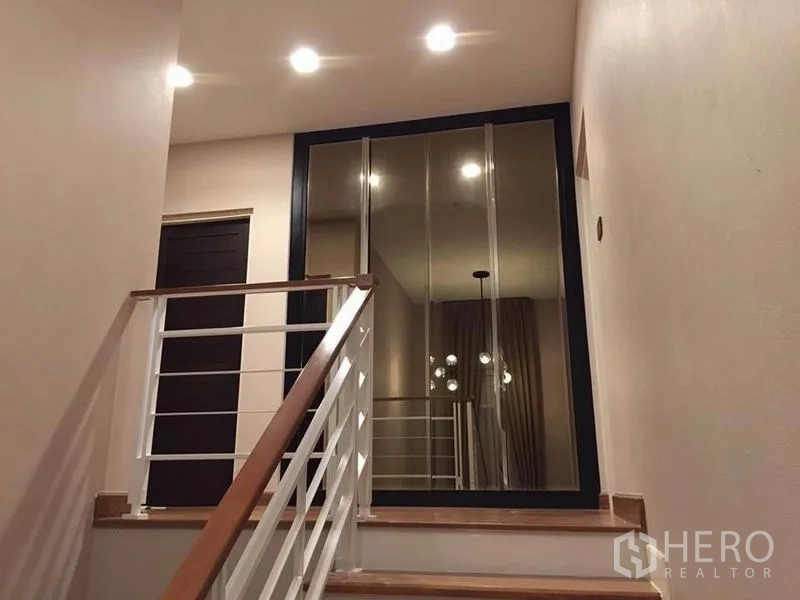 Detached House for rent or sale in Khlong Toei, Bangkok - Stair landing with white railing and full-height mirrored sliding doors in warm lighting.