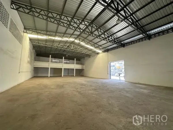Warehouse for rent in Mueang Pathum Thani, Pathum Thani - Clear-span warehouse interior with high steel truss roof, smooth concrete floor and a rear mezzanine for storage or office.