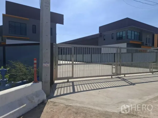 Factory for rent in Mueang Samut Sakhon, Samut Sakhon - Secure gated entrance with a large concrete yard between contemporary factory buildings.