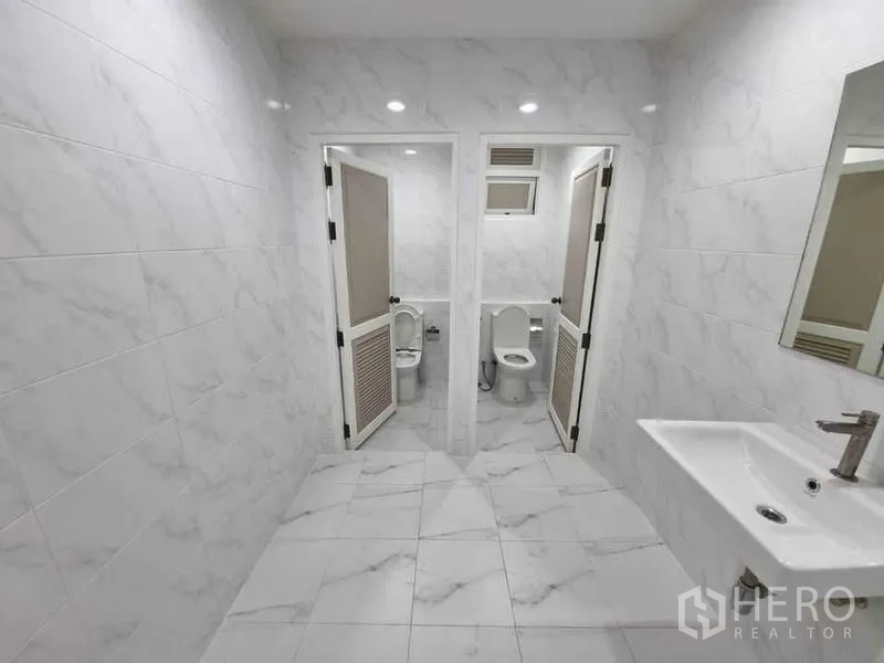 Shophouse for rent in Bang Rak, Bangkok - Bright bathroom with two toilet stalls, marble-look tiles and a wall-mounted basin.