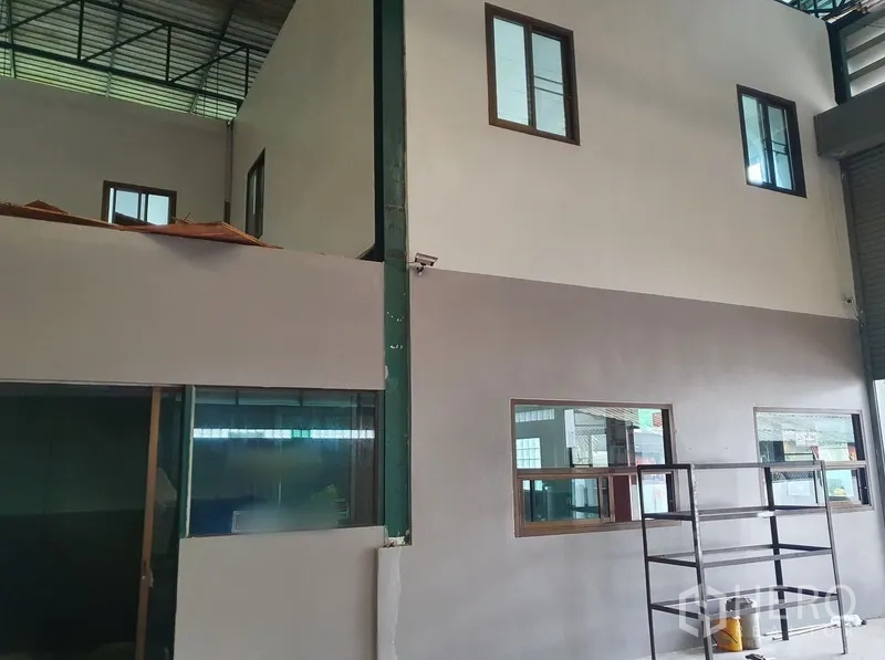 Factory for rent in Saphan Sung, Bangkok - Two‑storey internal office block with windows inside the warehouse and nearby shelving.