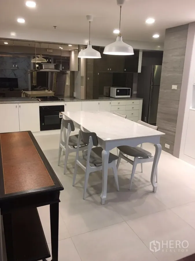 Condominium for rent in Watthana, Bangkok - Open-plan kitchen with white cabinetry, marble dining table, pendant lights, built-in oven and stainless fridge in a Sukhumvit condo.