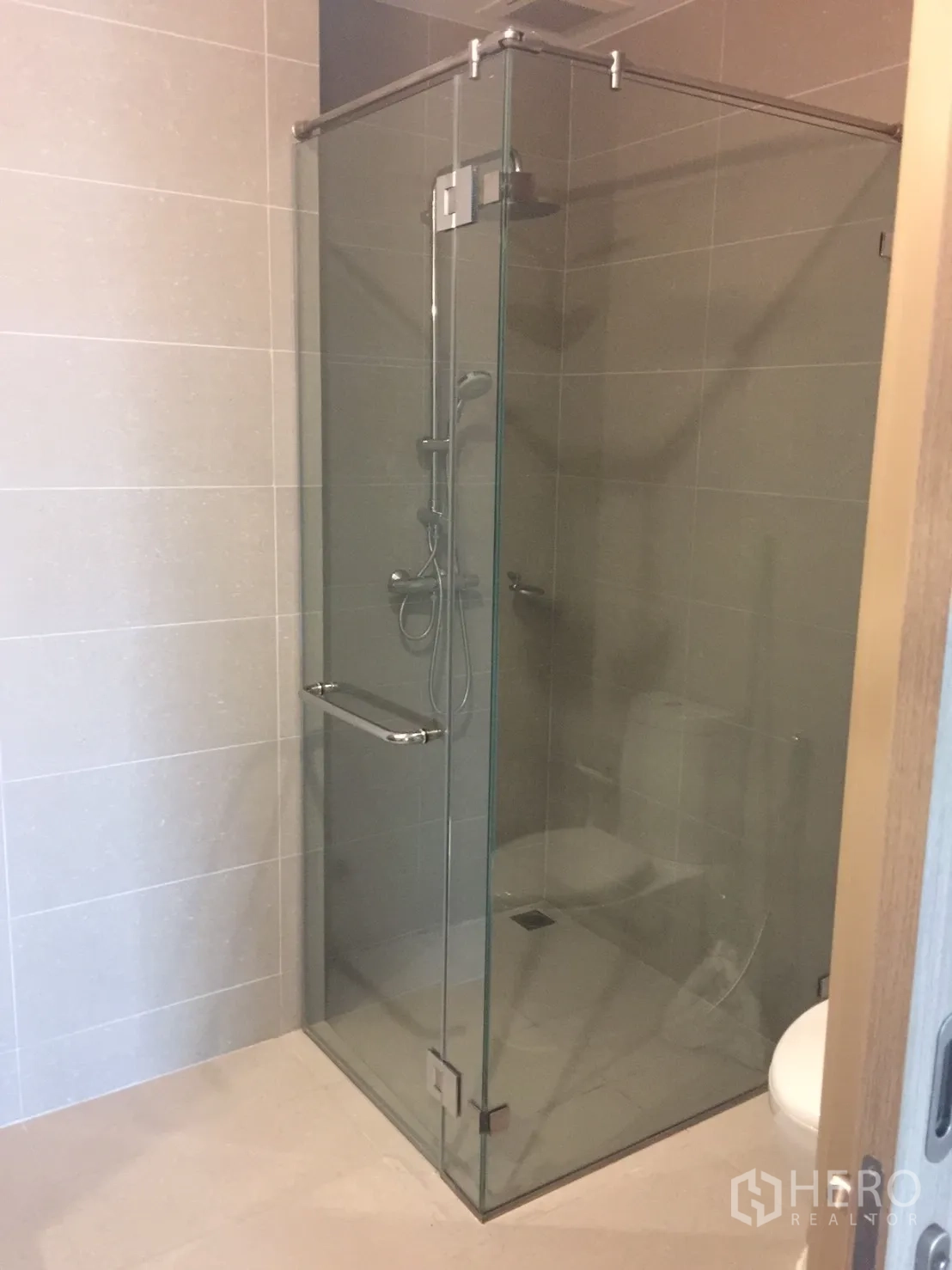 Condominium for rent in Pathum Wan, Bangkok - Glass-enclosed shower with handheld showerhead in a tiled bathroom.
