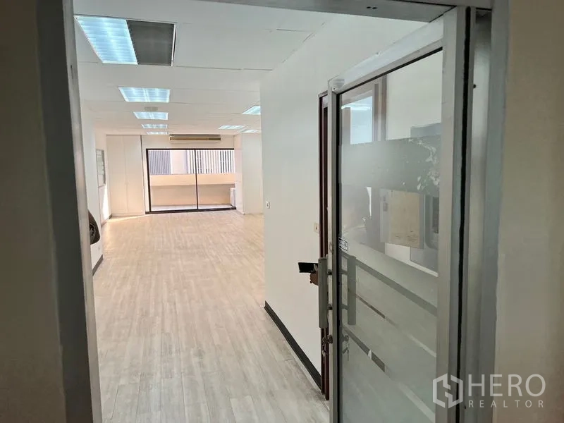 Office Space for rent in Pathum Wan, Bangkok - View from glass entry door into long office hall with ceiling panels and a balcony at the end.