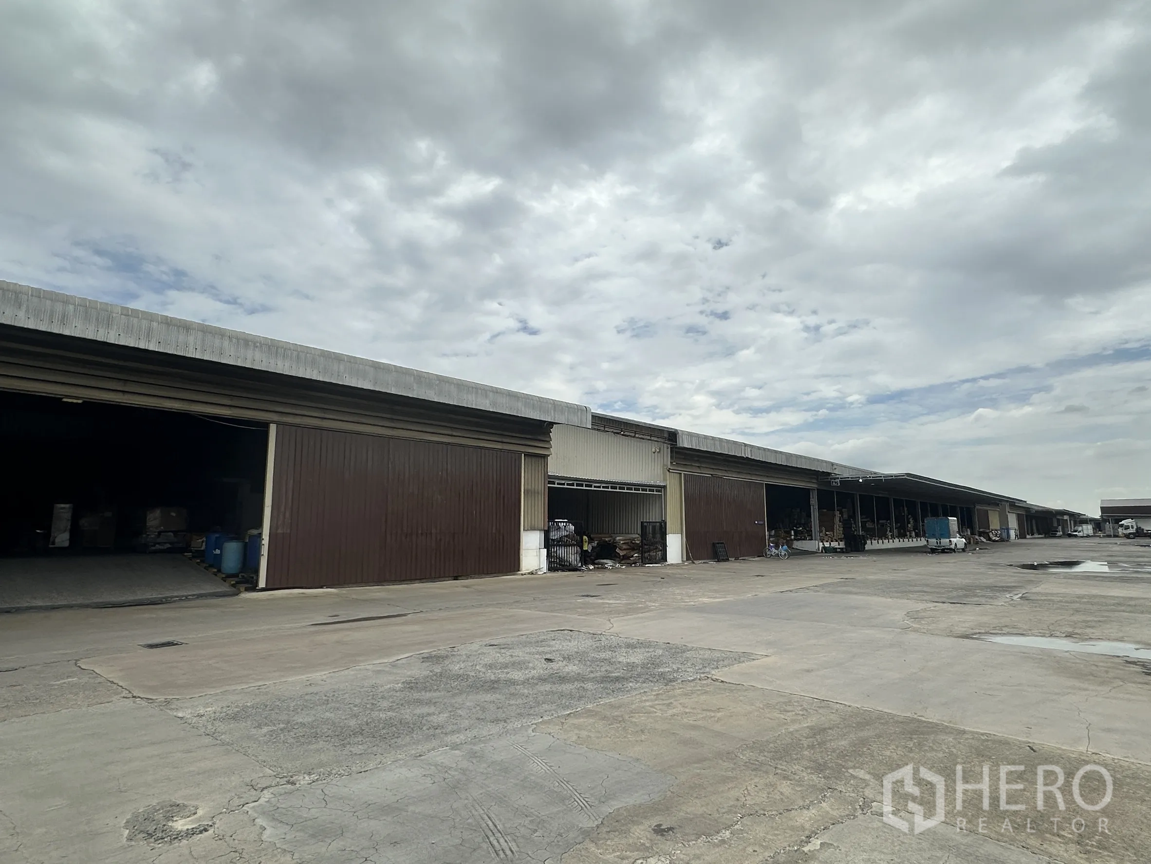 Factory for rent in Lat Krabang, Bangkok - Row of adjoining warehouse units with roller shutters and a broad paved driveway.