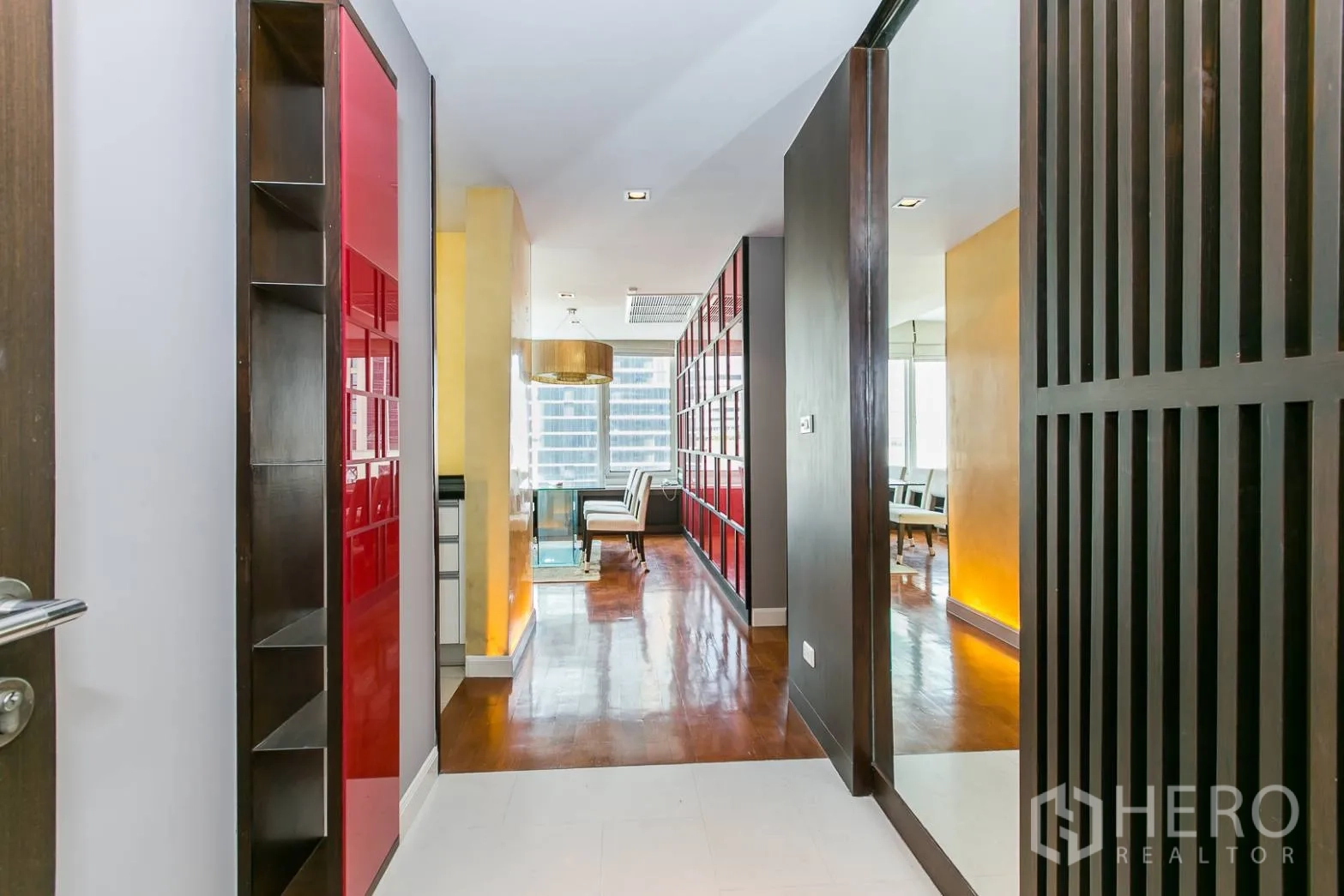 Condominium for rent or sale in Khlong Toei, Bangkok - Entry corridor with red panel shelving, mirror and wood floors leading to living area.