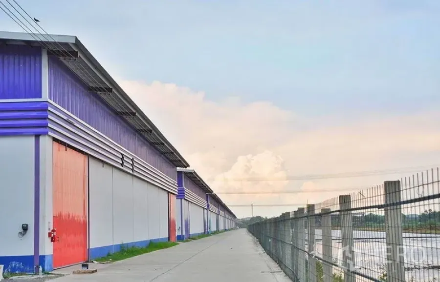 คลังสินค้า ให้เช่าในPathum Thani - มุมมองด้านข้างโกดังประตูแดงเรียงต่อกัน รั้วรอบโครงการ ถนนบริการและคลองระบายน้ำ