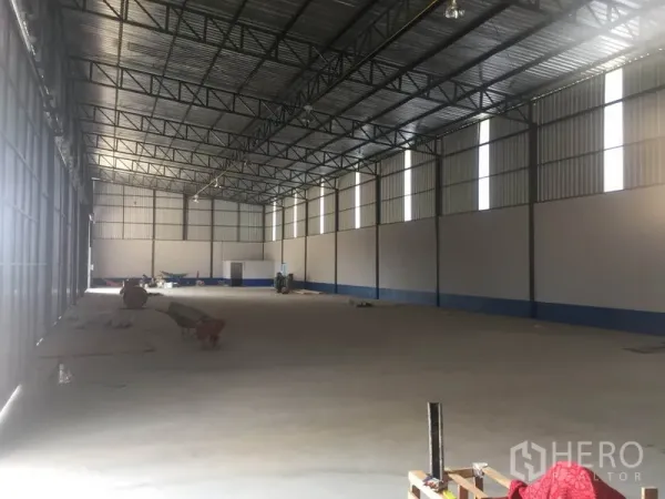 Warehouse for rent in Sai Mai, Bangkok - Open-plan warehouse space with metal truss roof, tall windows and clear floor area for storage.