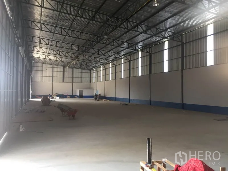 Warehouse for rent in Sai Mai, Bangkok - Open-plan warehouse space with metal truss roof, tall windows and clear floor area for storage.