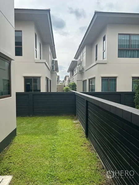 Detached House for rent in Bang Kapi, Bangkok - Backyard lawn between black privacy fences and neighboring houses.