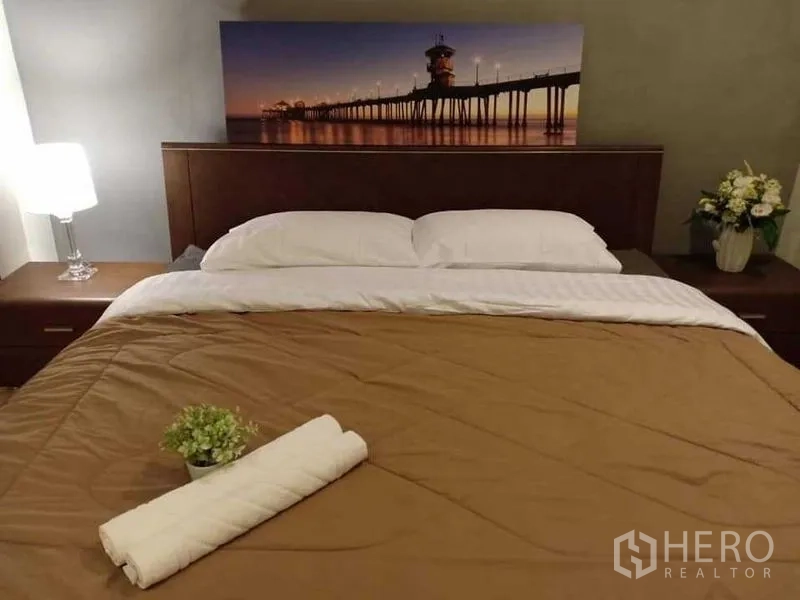 Condominium for rent in Khlong Luang, Pathum Thani - Cozy master bedroom with king bed, bedside lamps and wall art.