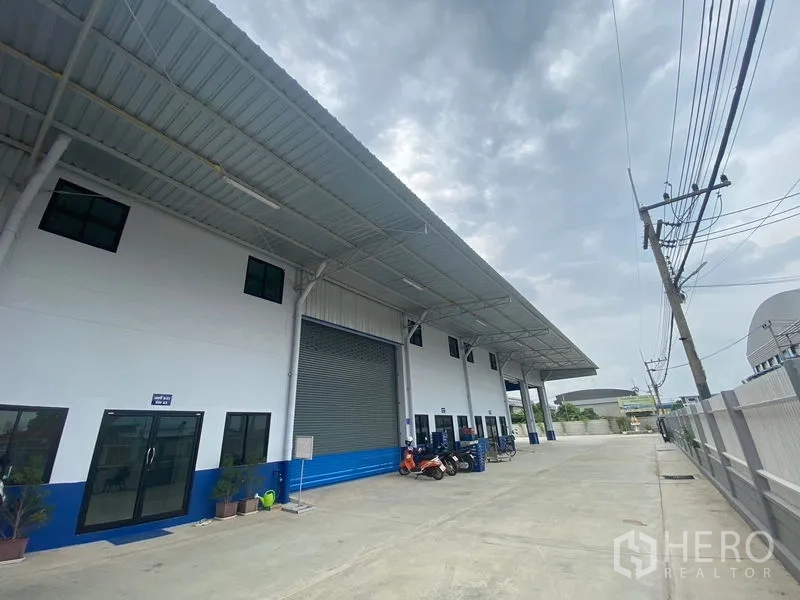 货栈 出租在Pathum Thani - 正面外立面，卷帘门、玻璃办公室门与宽阔硬地。