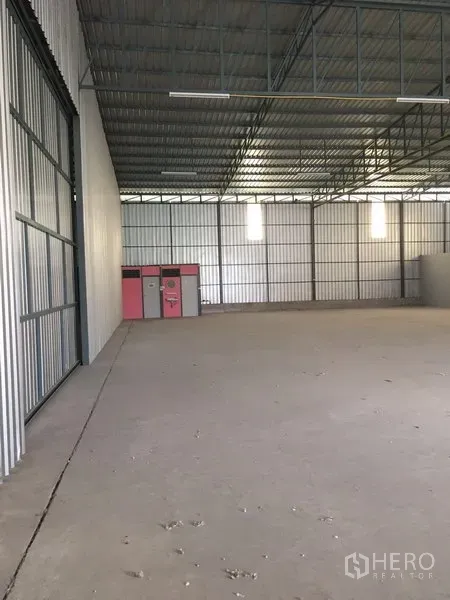 Warehouse for rent in Bang Kapi, Bangkok - Open warehouse space with large sliding steel entrance, concrete flooring, lockers along the wall and high truss ceiling.