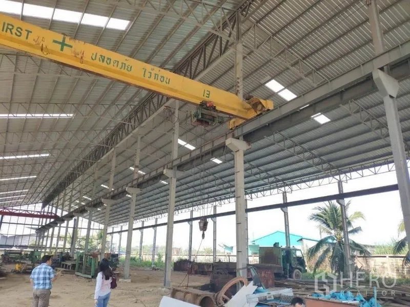 Factory for rent in Samut Sakhon - Detail of a yellow overhead crane inside the warehouse with palm trees outside in Samut Sakhon.