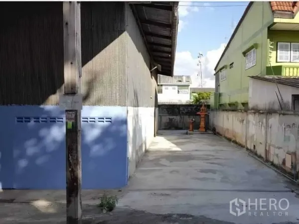 货栈 出租在Sai Noi, Nonthaburi - 仓库侧面混凝土空地，围墙与蓝色门