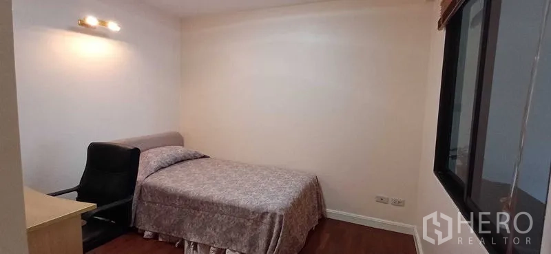 Condominium for sale in Pathum Wan, Bangkok - Cozy second bedroom with double bed, desk chair, wall light and hardwood flooring in a Bangkok condominium.