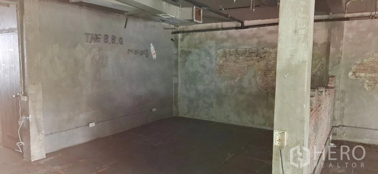 Shophouse for rent or sale in Watthana, Bangkok - Spacious room with concrete walls, ceiling pipes, and rough brick sections ready for fit-out.
