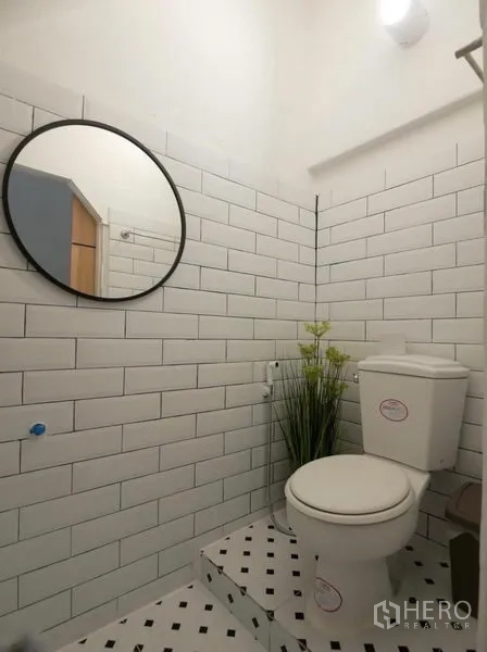 Townhouse for rent in Khlong Toei, Bangkok - Small powder room with white subway tiles, a round mirror, raised step and toilet.