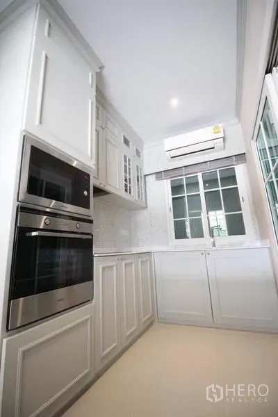 Detached House for rent or sale in Lat Phrao, Bangkok - Compact white kitchen with built-in oven, paneled cabinets and window.