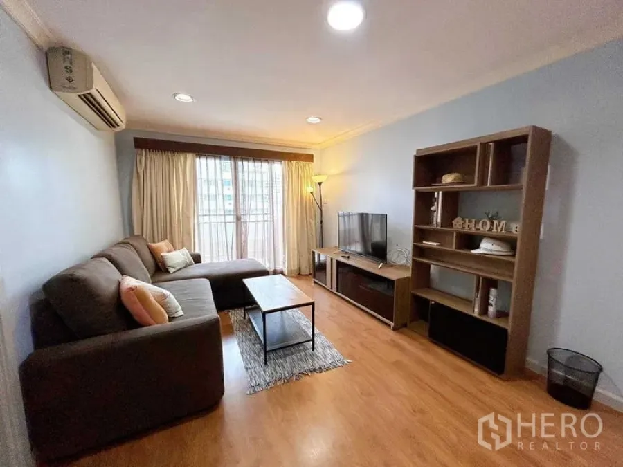 Condominium for rent in Watthana, Bangkok - Living area with TV and shelving facing balcony doors with sheer curtains.