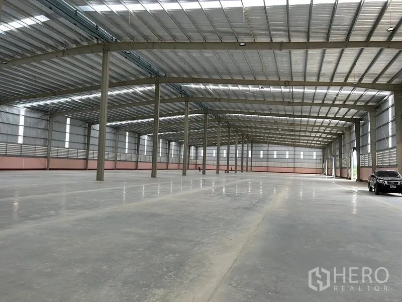 Warehouse for rent in Nikhom Phatthana, Rayong - Open-plan storage hall with wide column spacing and vehicle access visible at the far end.