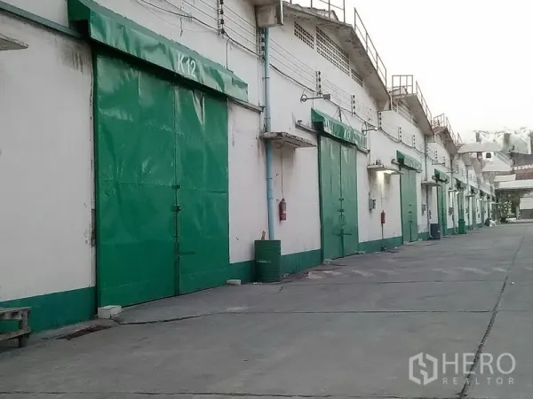 Warehouse for rent in Khlong Toei, Bangkok - Close view of green metal warehouse doors and utilities along a service lane in an industrial compound.