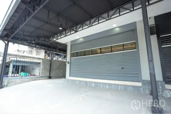 Home Office for rent in Bang Khen, Bangkok - Covered carport with metal roof and wide roller shutter frontage ideal for a showroom or loading.
