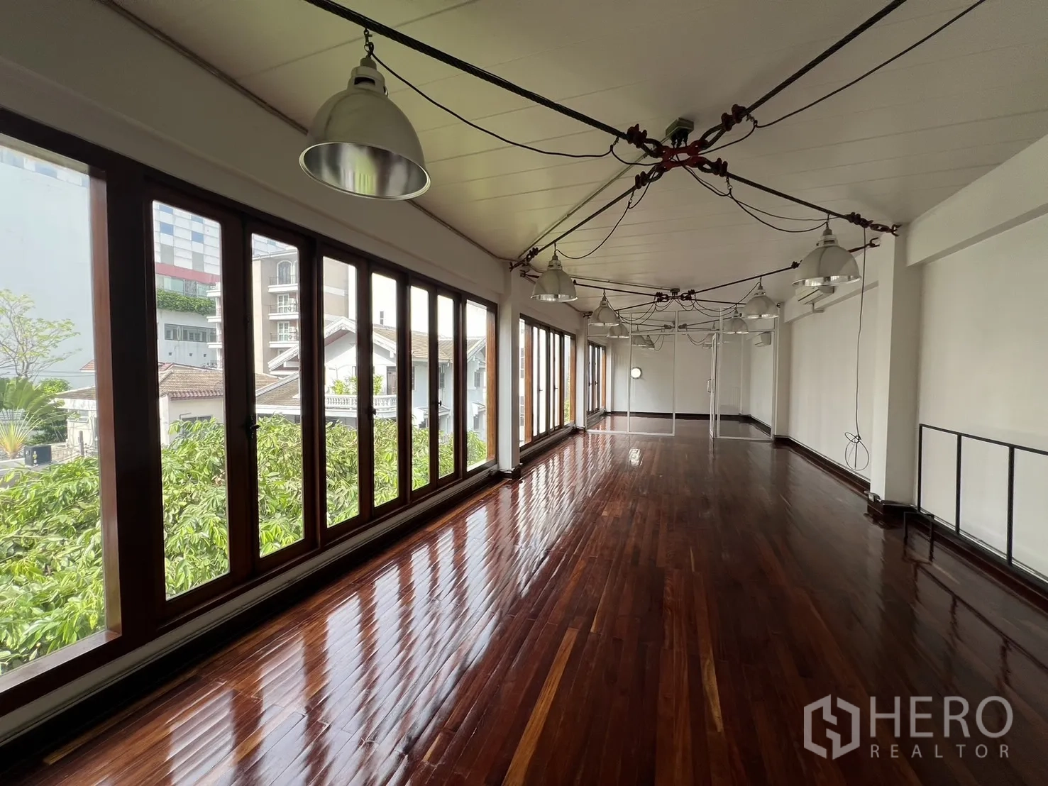 Home Office for rent in Watthana, Bangkok - Light-filled studio space with continuous windows, exposed cable lighting and dark wood floors.