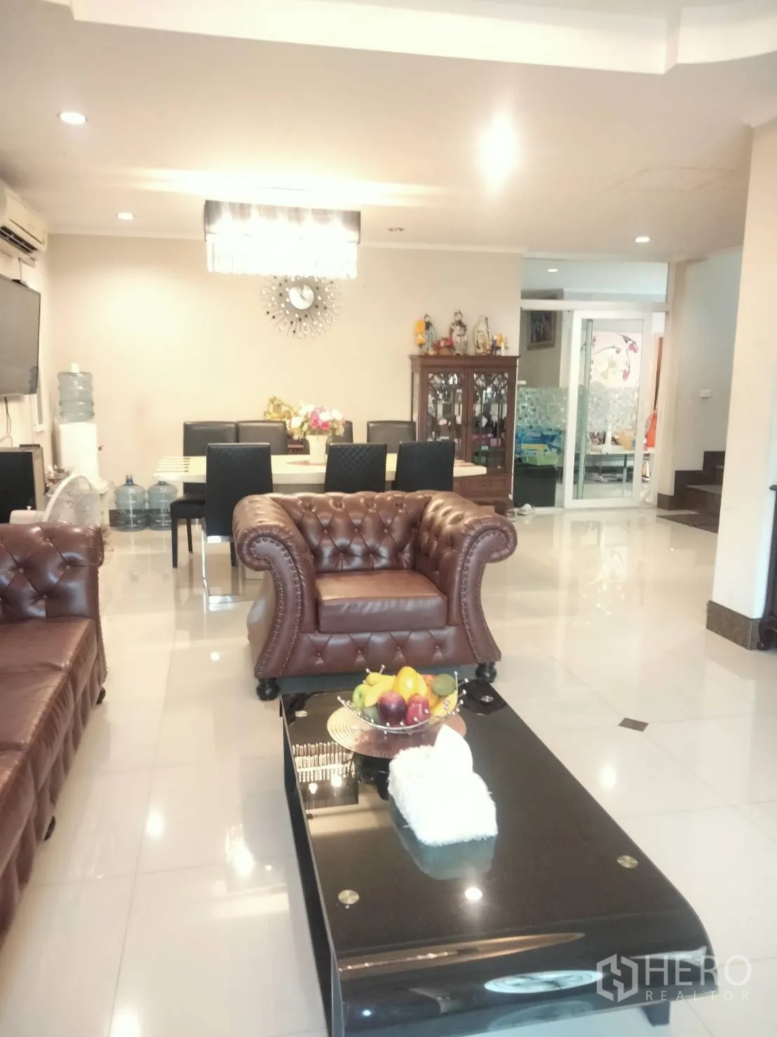 独栋房屋 for rent in Pak Kret, Nonthaburi - 明亮的开放式客餐厅，配棕色皮沙发、吊灯与亮面地砖。