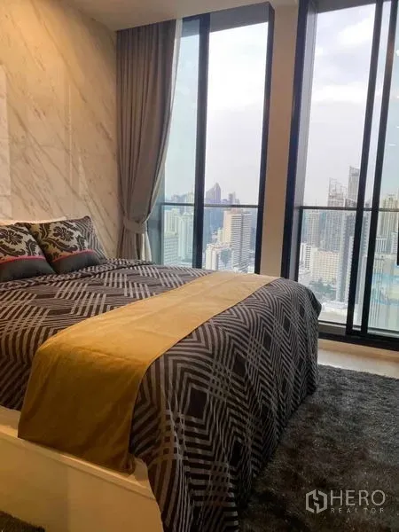 Condominium for sale in Pathum Wan, Bangkok - Bedroom with marble accent wall and floor-to-ceiling windows overlooking the Bangkok skyline.