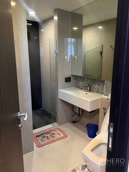 Condominium for rent in Khlong Toei, Bangkok - Contemporary bathroom featuring a glass shower enclosure, large mirror and wall-mounted basin.