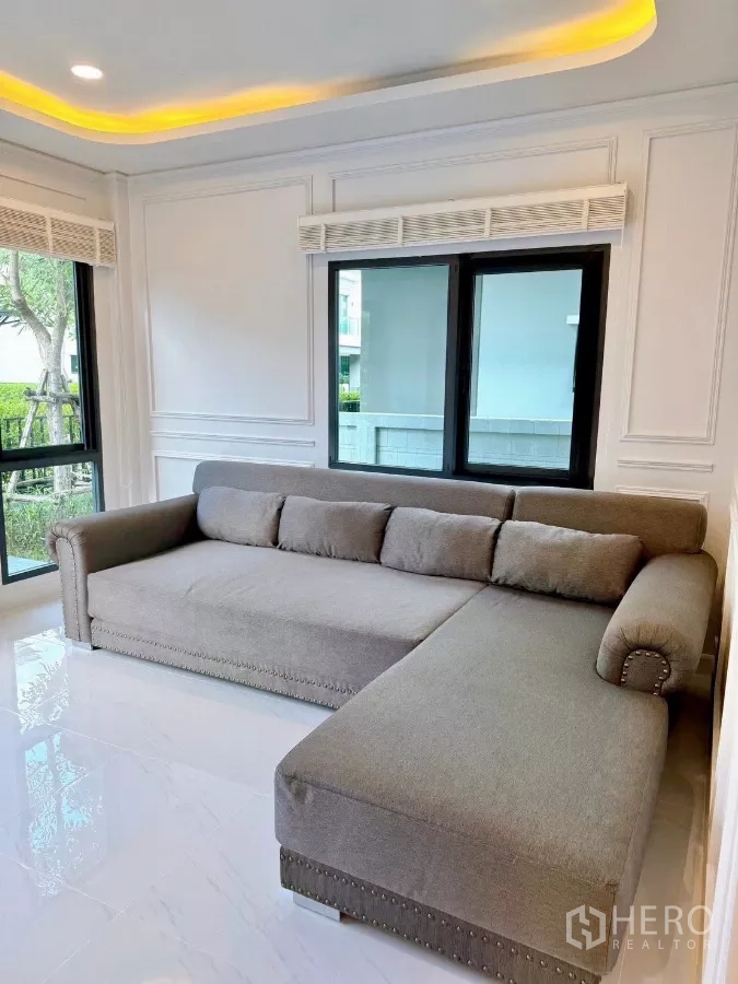 Detached House for rent in Bang Phli, Samut Prakan - Corner of the living area featuring a large upholstered L-shaped sofa beside windows and recessed lights.